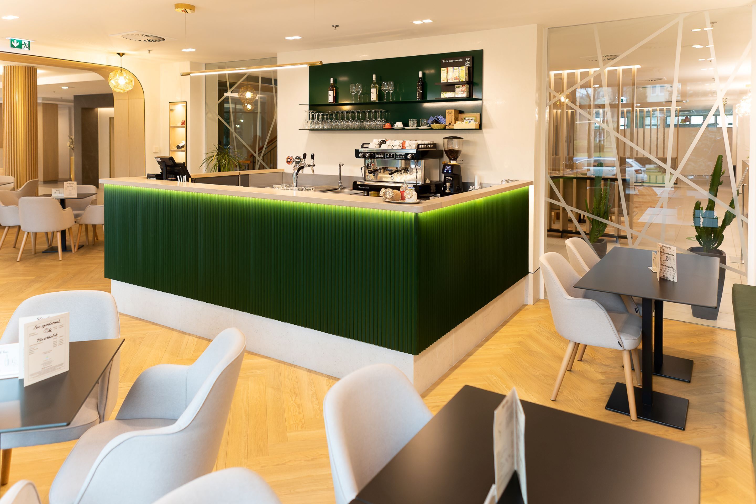 Zona de bar moderna con mostrador verde, asientos y una máquina de café.