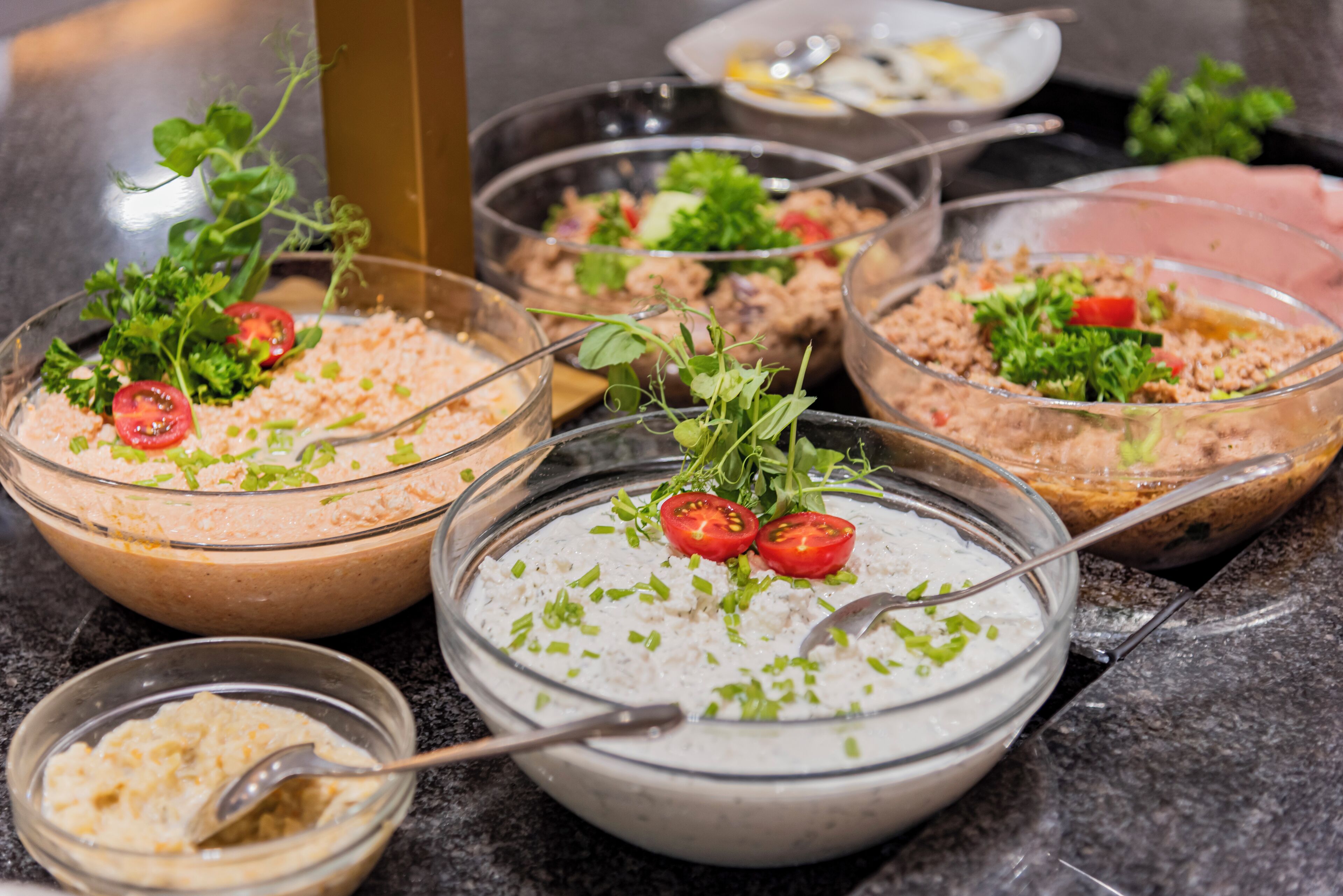 A variety of dishes with garnishes, including a bowl with a creamy white sauce, a bowl with a brownish mixture, and a bowl with a pinkish mixture.