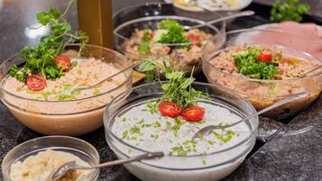 A variety of dishes with garnishes, including a bowl with a creamy white sauce, a bowl with a brownish mixture, and a bowl with a pinkish mixture.