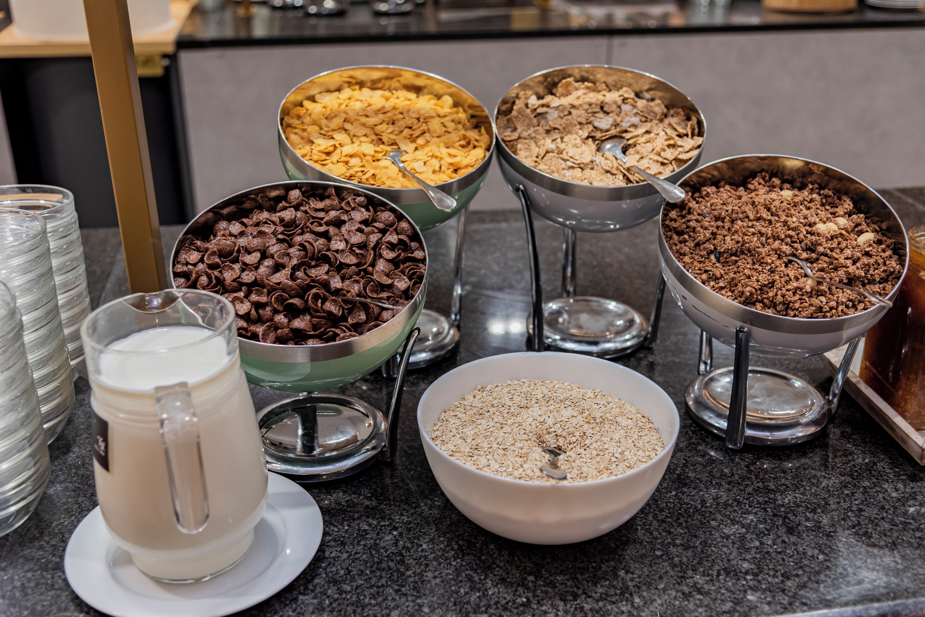 Mesa de buffet com diversos alimentos, incluindo cereais, gotas de chocolate e leite.