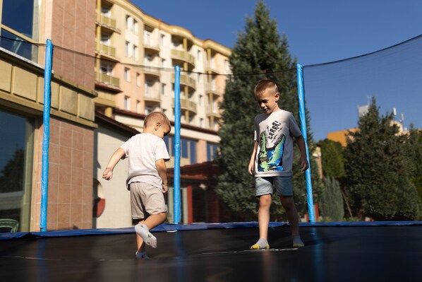Two children playing on a trampoline in front of a building with multiple balconies. - Hotel Karos Spa (Zalakaros)