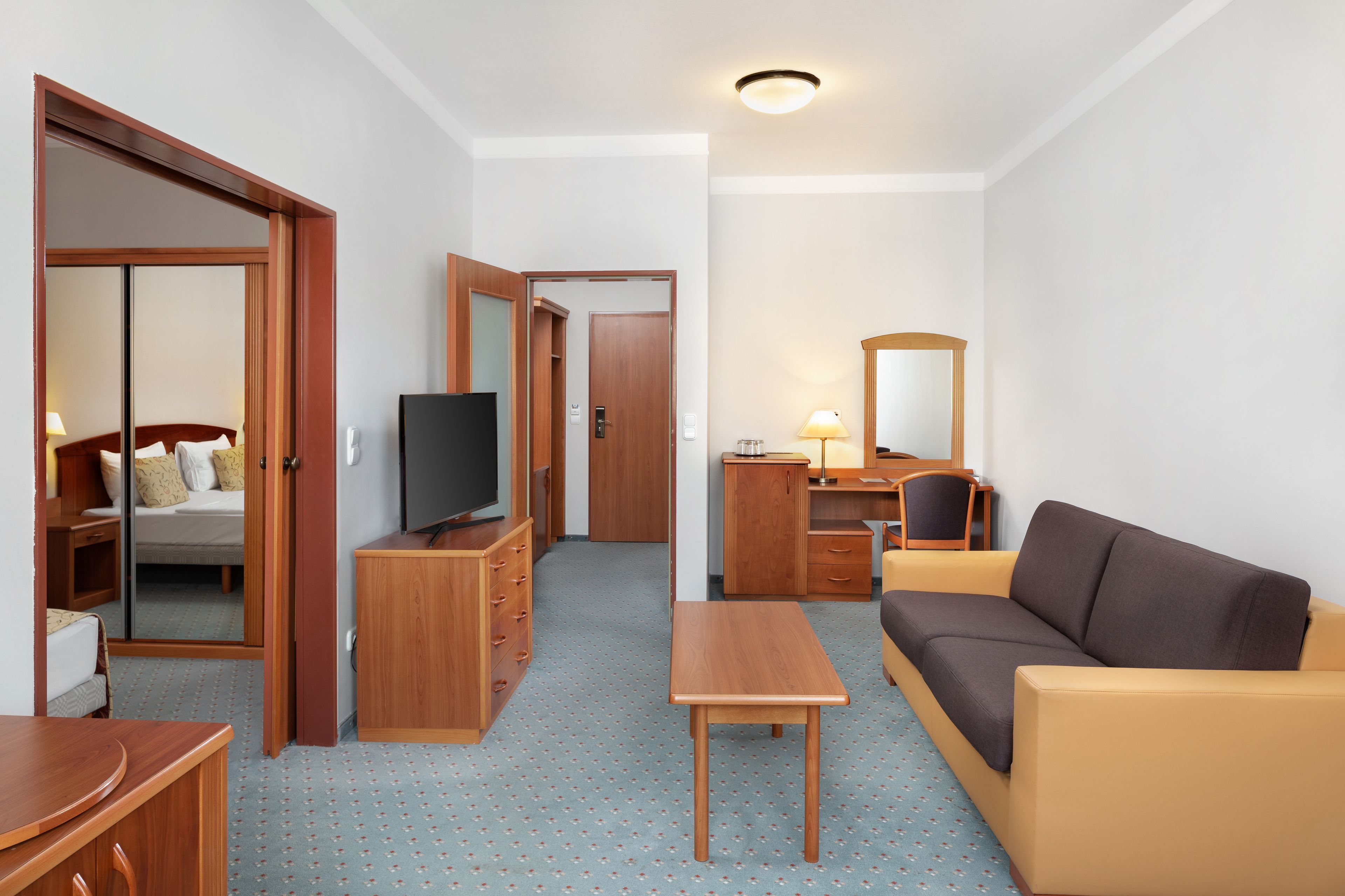 Ein kleines Hotelzimmer mit Bett, Fernseher, Schreibtisch, Schlafsofa und Spiegel.