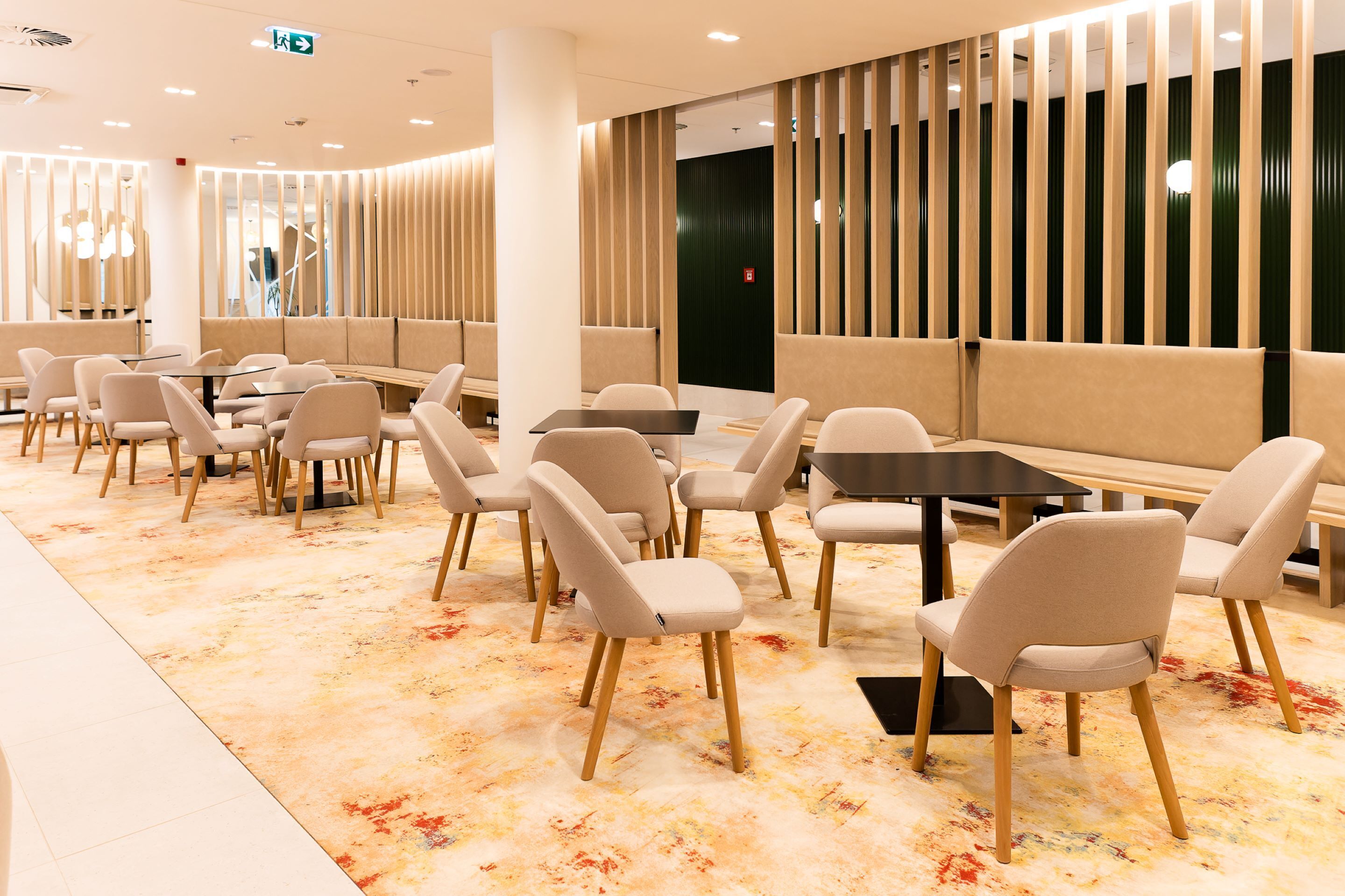 A modern restaurant with booths and tables, a patterned carpet, and a decorative wall with vertical panels.