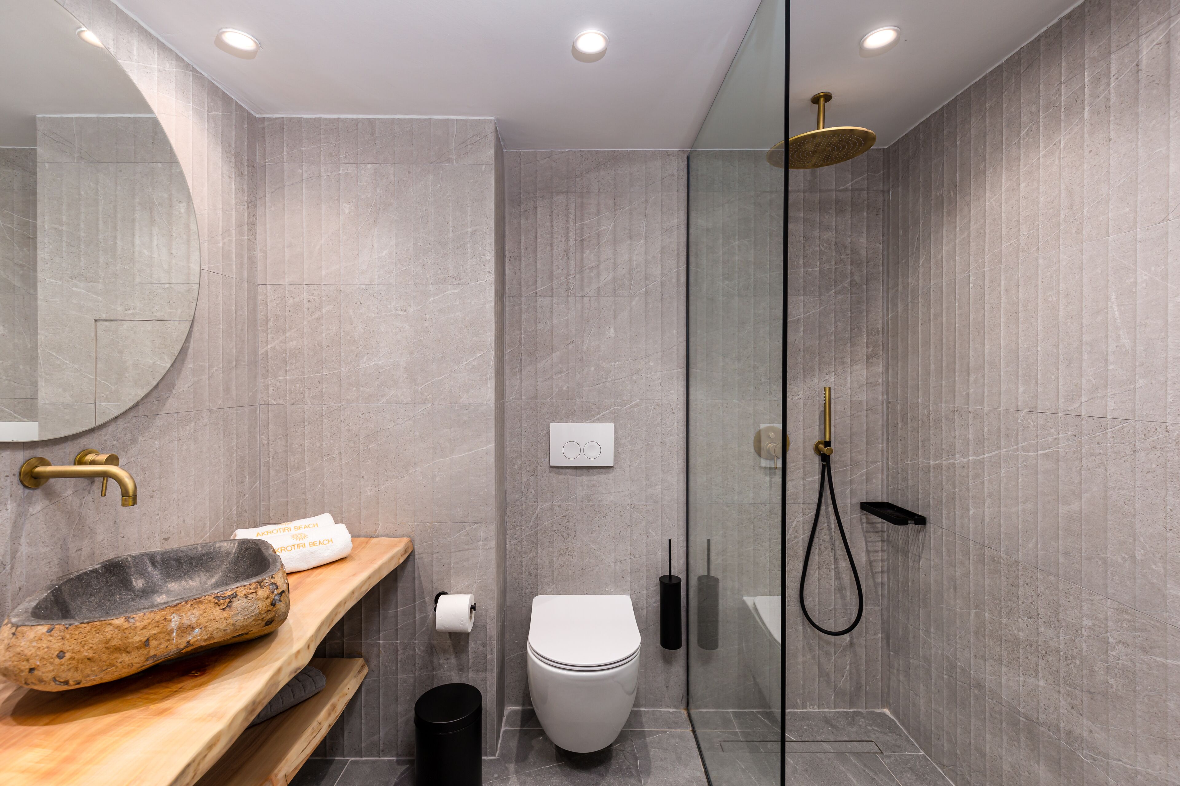 Een moderne badkamer met een wastafel van steen, toilet en een douchecabine met glazen wanden.