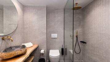 Een moderne badkamer met een wastafel van steen, toilet en een douchecabine met glazen wanden.