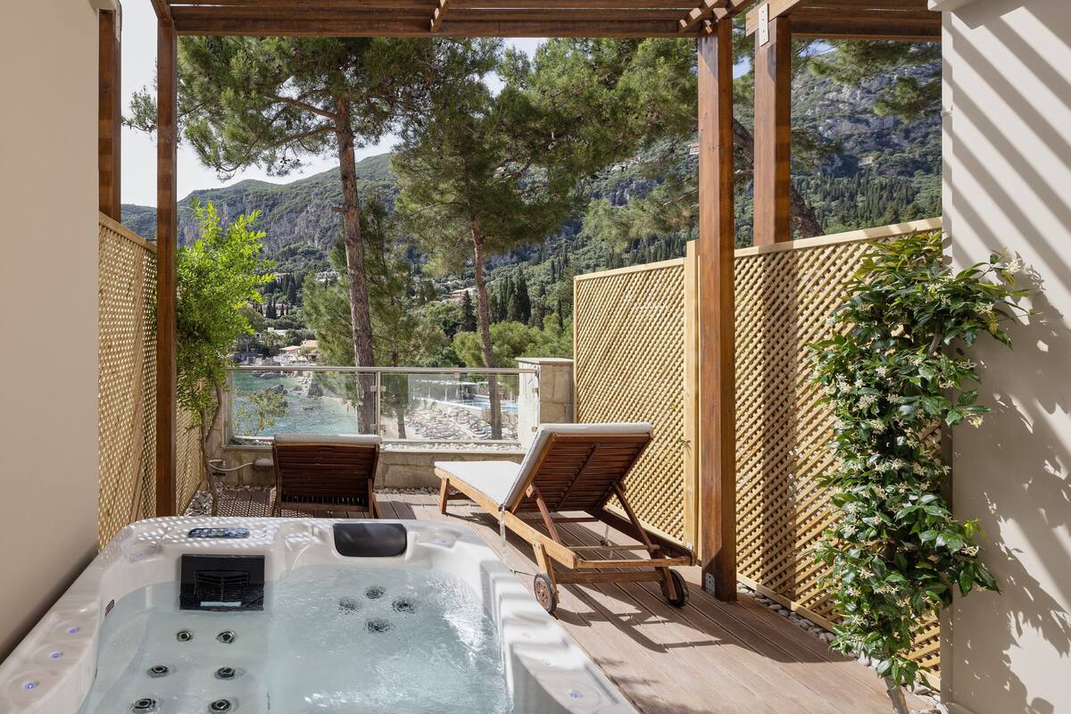 Un bain à remous avec deux chaises longues, une terrasse en bois et une vue sur un paysage montagneux.