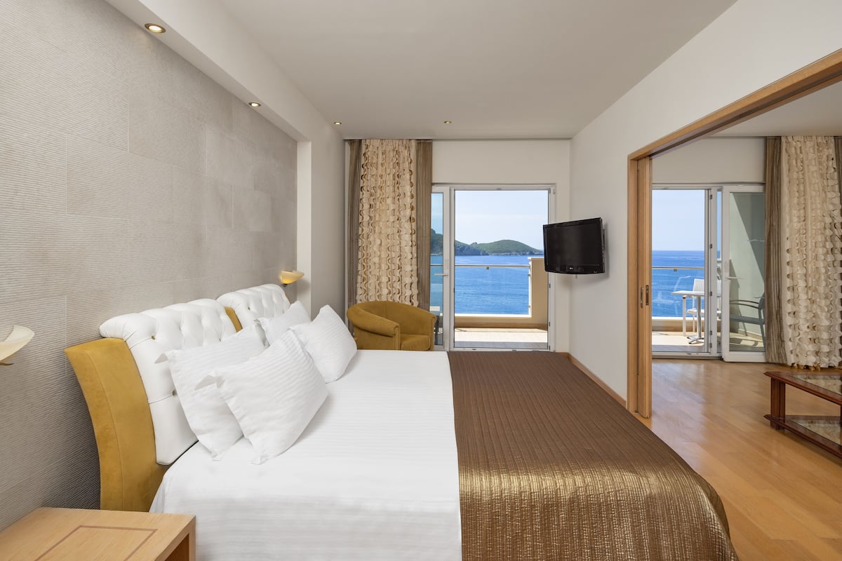 A hotel room with a large bed, a sofa, a TV, and a view of the sea.