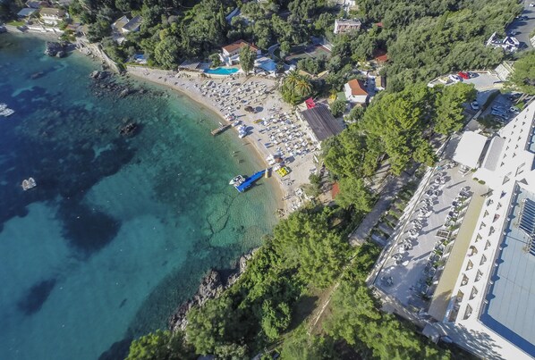 Vista aérea de una zona costera con playa, aguas cristalinas y un estacionamiento.