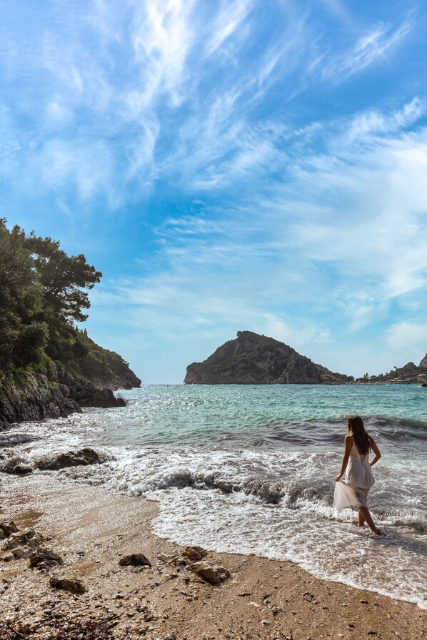 A beach with rocky terrain and a woman in a white dress walking towards the water. - Akrotiri Beach Resort & Spa - Adult Friendly (Corfu)