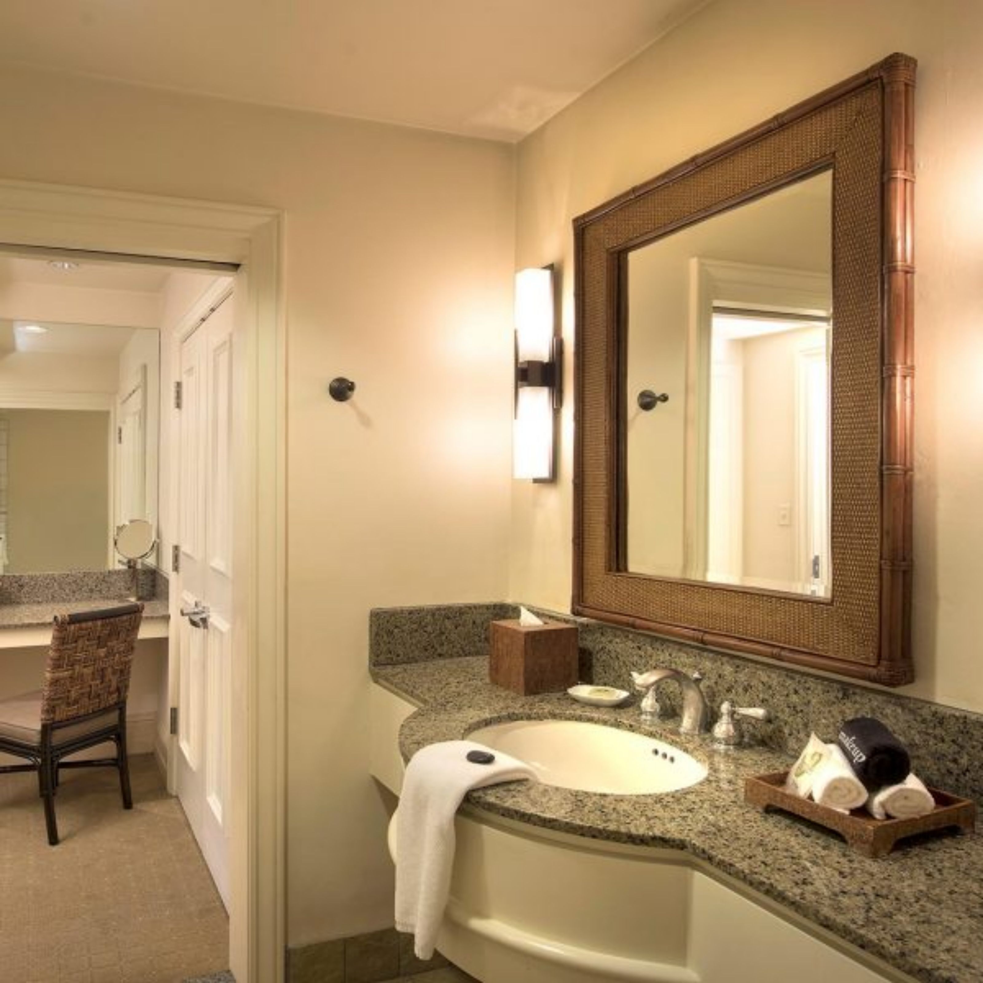 Ein Hotelbad mit einem großen Spiegel, einem Waschbecken, einem Handtuch und Toilettenartikeln.