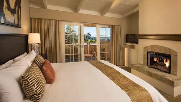 A hotel room with a large bed, a fireplace, and a balcony with curtains. - Tradewinds Carmel (Carmel)