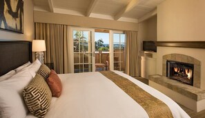 A hotel room with a large bed, a fireplace, and a balcony with curtains. - Tradewinds Carmel (Carmel)