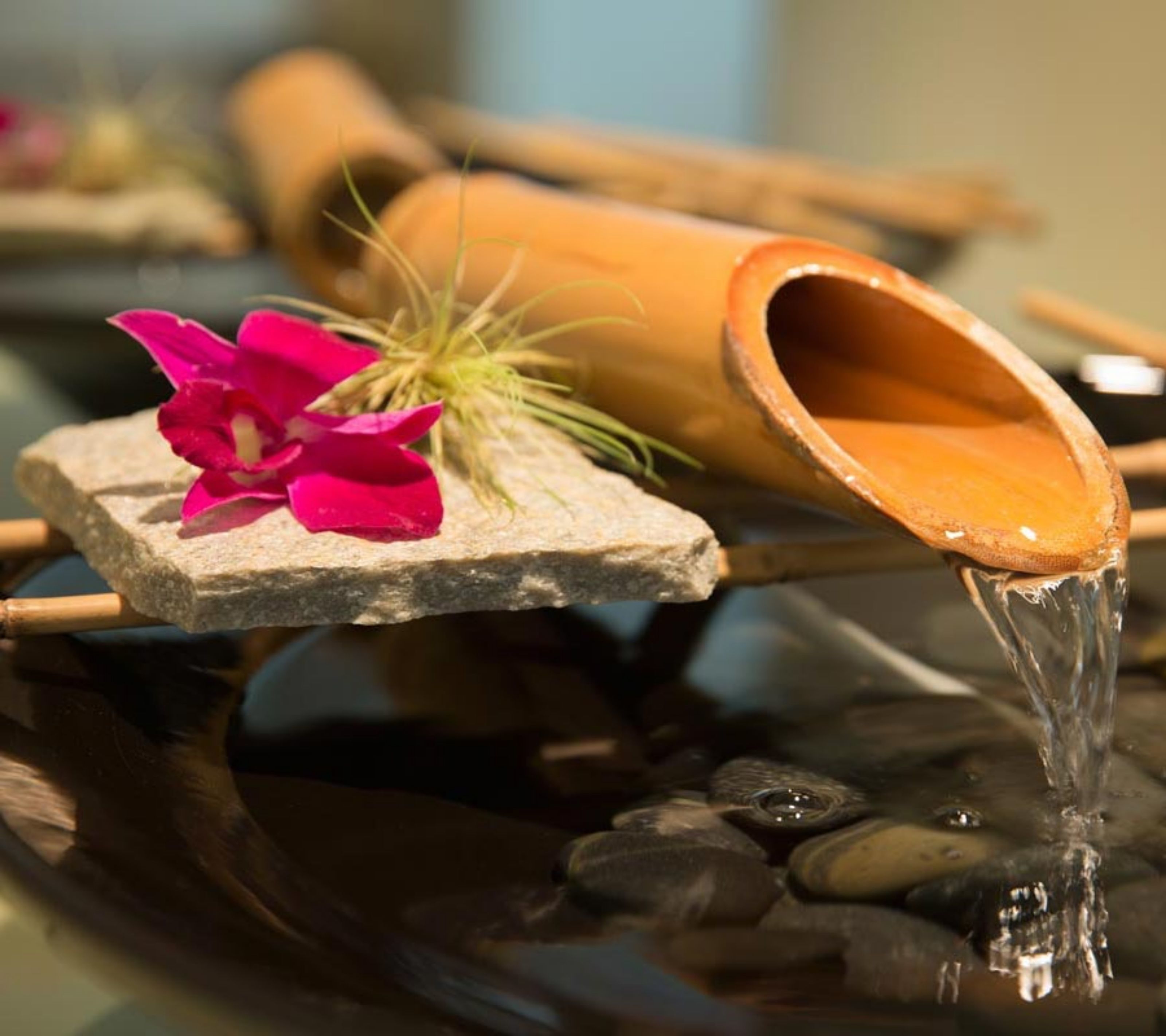 A water feature with a stone base, a pink flower, and a bamboo container.