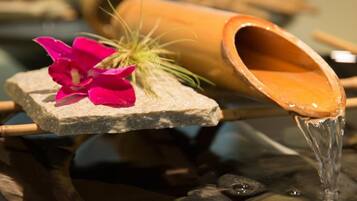A water feature with a stone base, a pink flower, and a bamboo container.