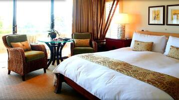 Quarto de hotel com uma cama grande, duas cadeiras, uma mesinha e um abajur.