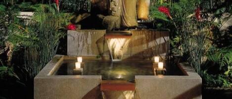 A large Buddha statue in a garden setting with a water feature and candles.