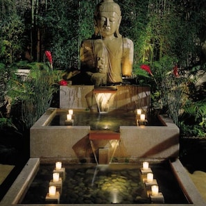 A large Buddha statue in a garden setting with a water feature and candles.