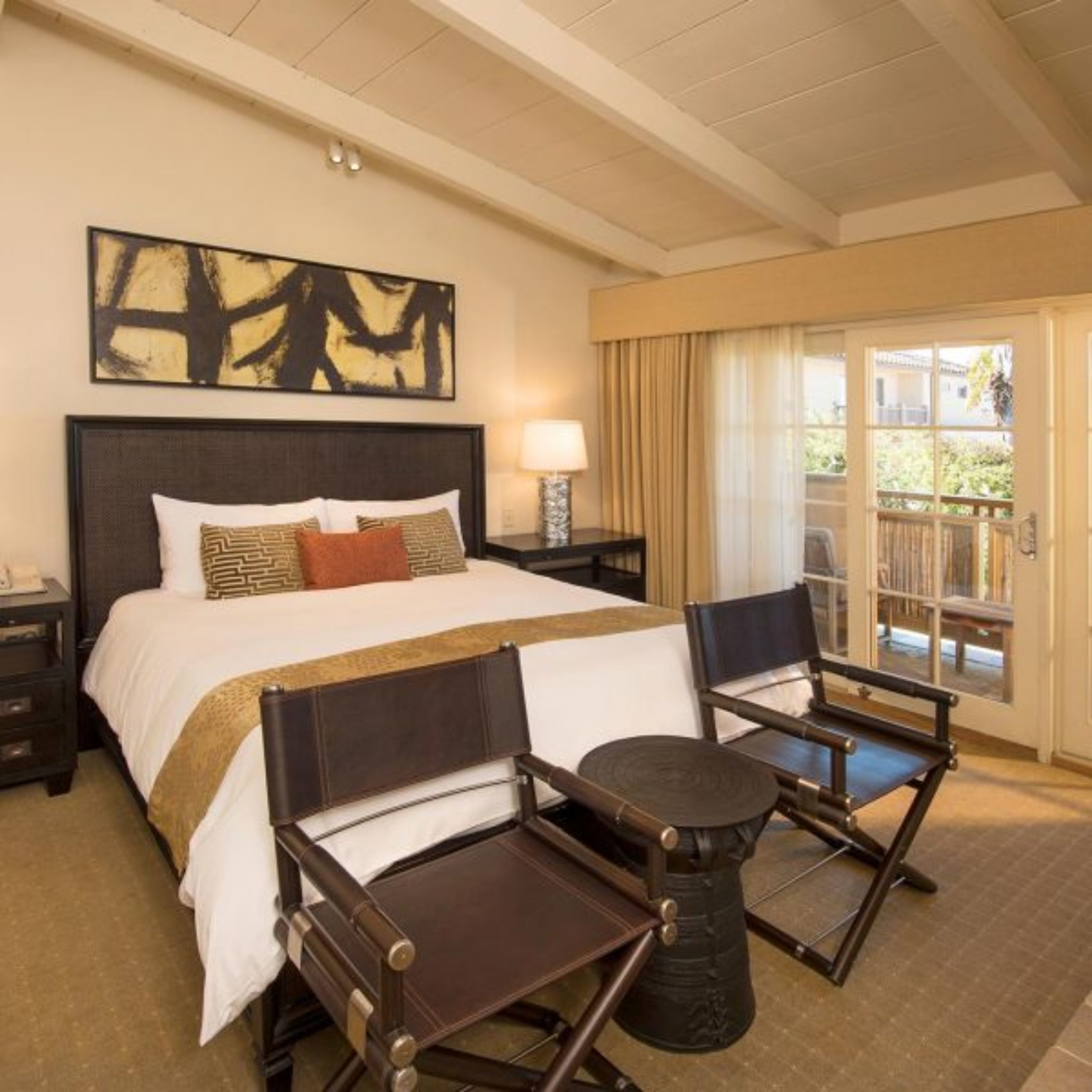 A hotel room with a large bed, two chairs, a small table, a nightstand, a lamp, and a painting on the wall.