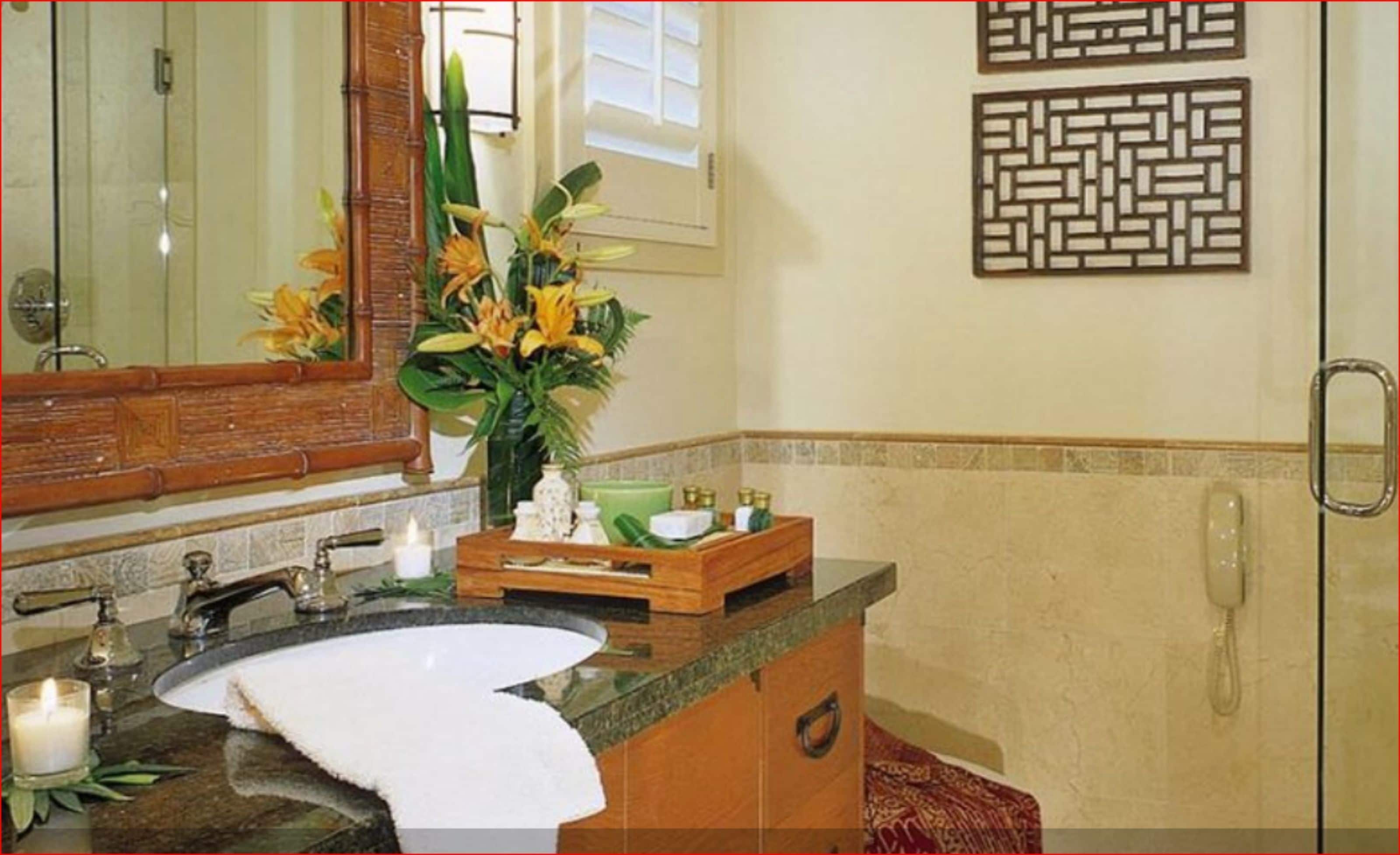 Un baño con lavamanos, espejo y un florero decorativo con flores.