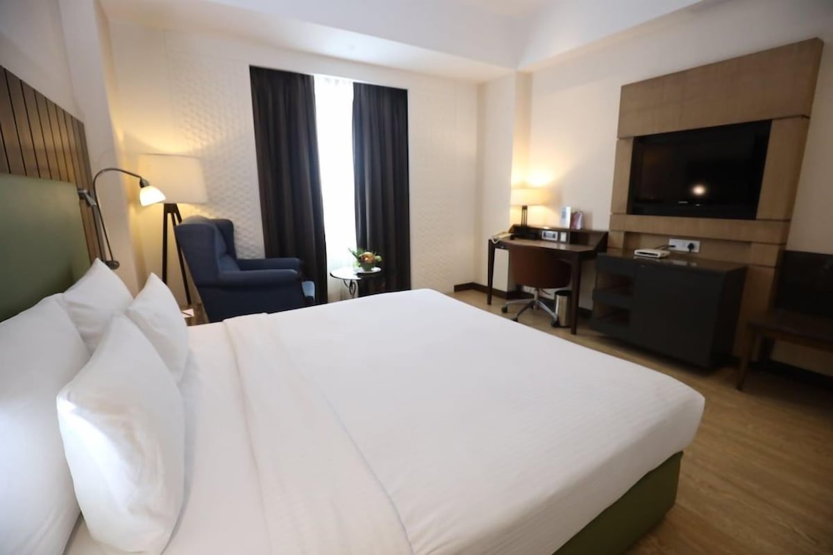 Ein Hotelzimmer mit einem großen Bett, einem Schreibtisch, einem Stuhl, einem Fernseher und einer Lampe.