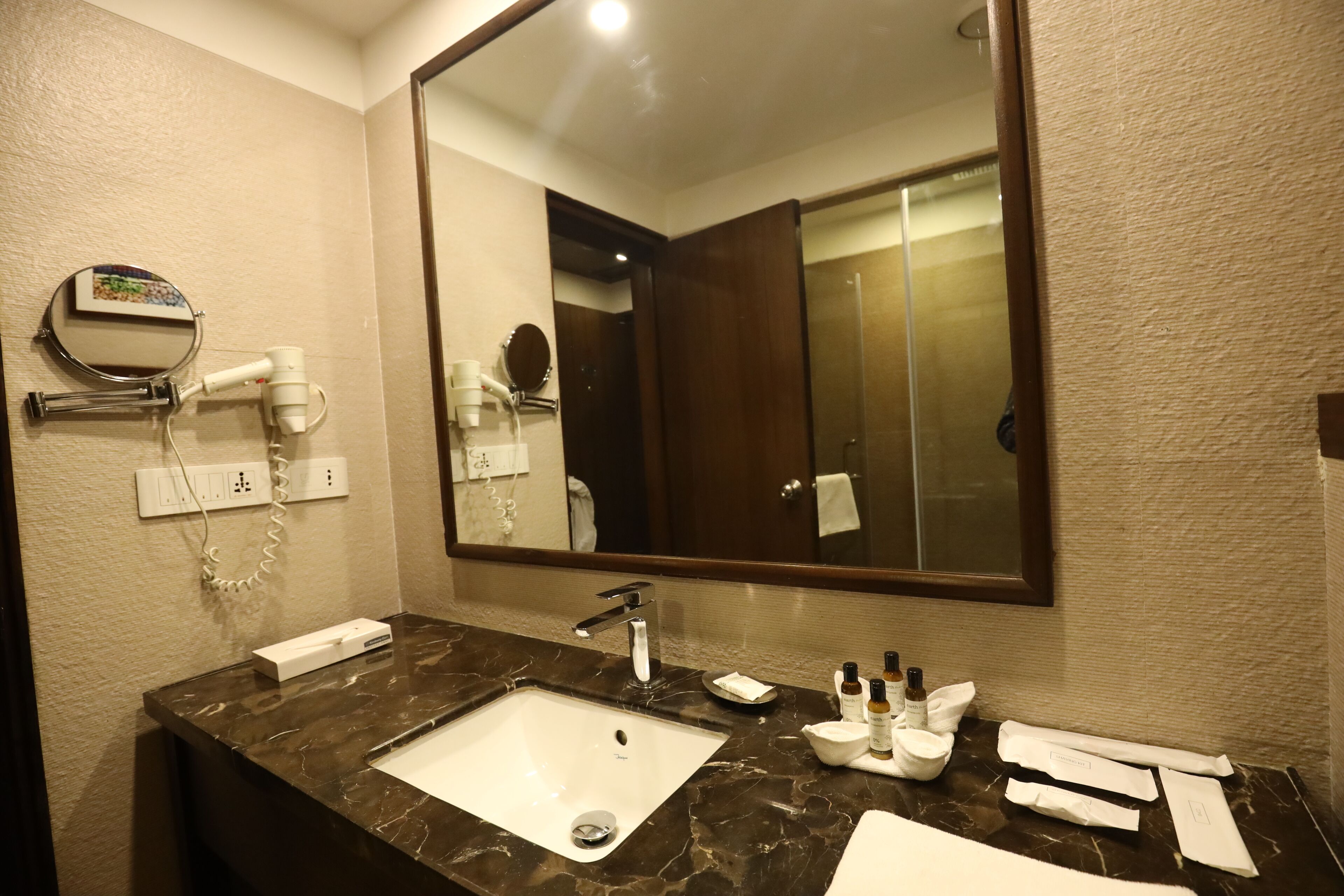 A bathroom with a marble sink, a large mirror, a hairdryer, and toiletries on the counter.