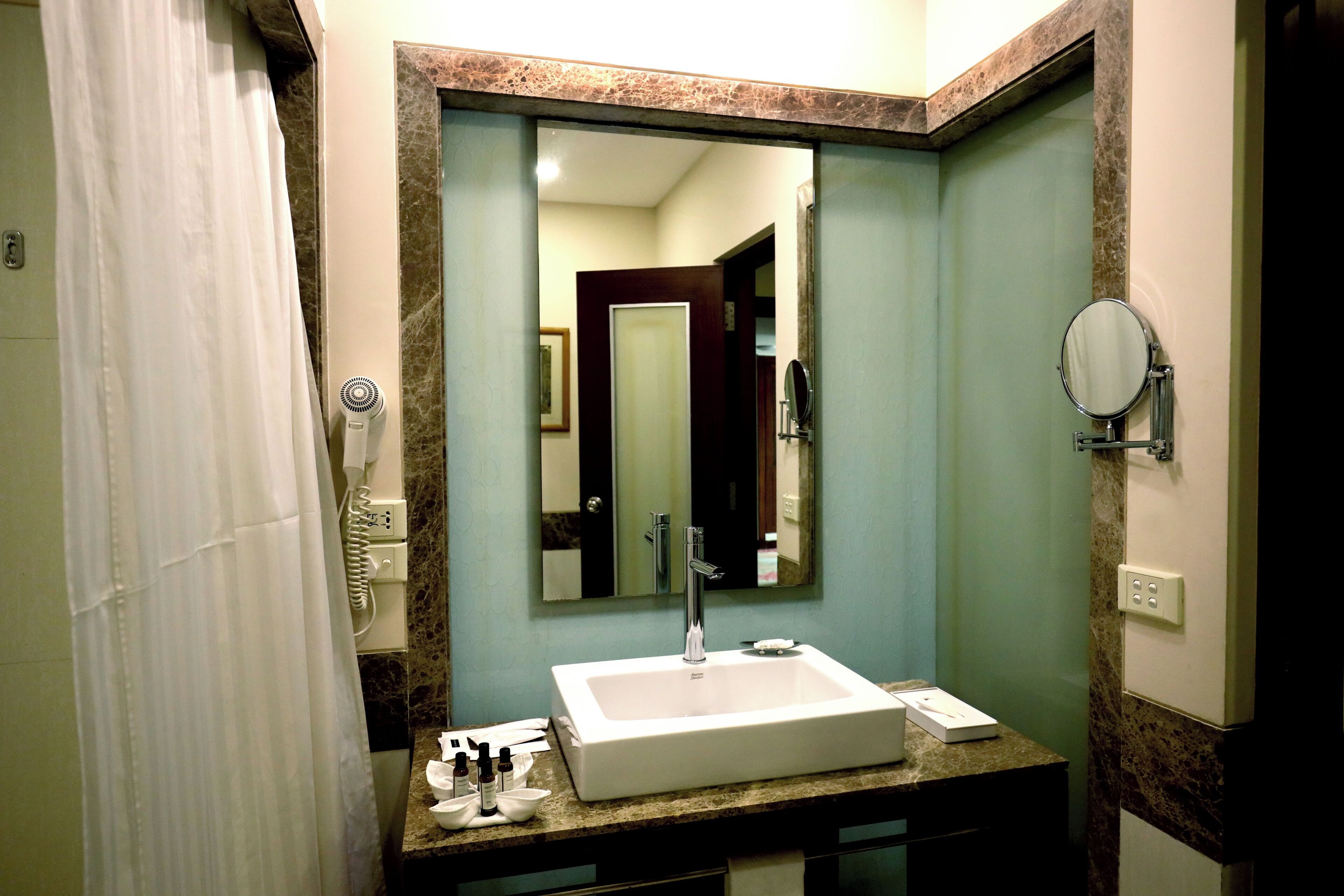 A bathroom with a white sink, a large mirror, a hairdryer, and a towel rack.