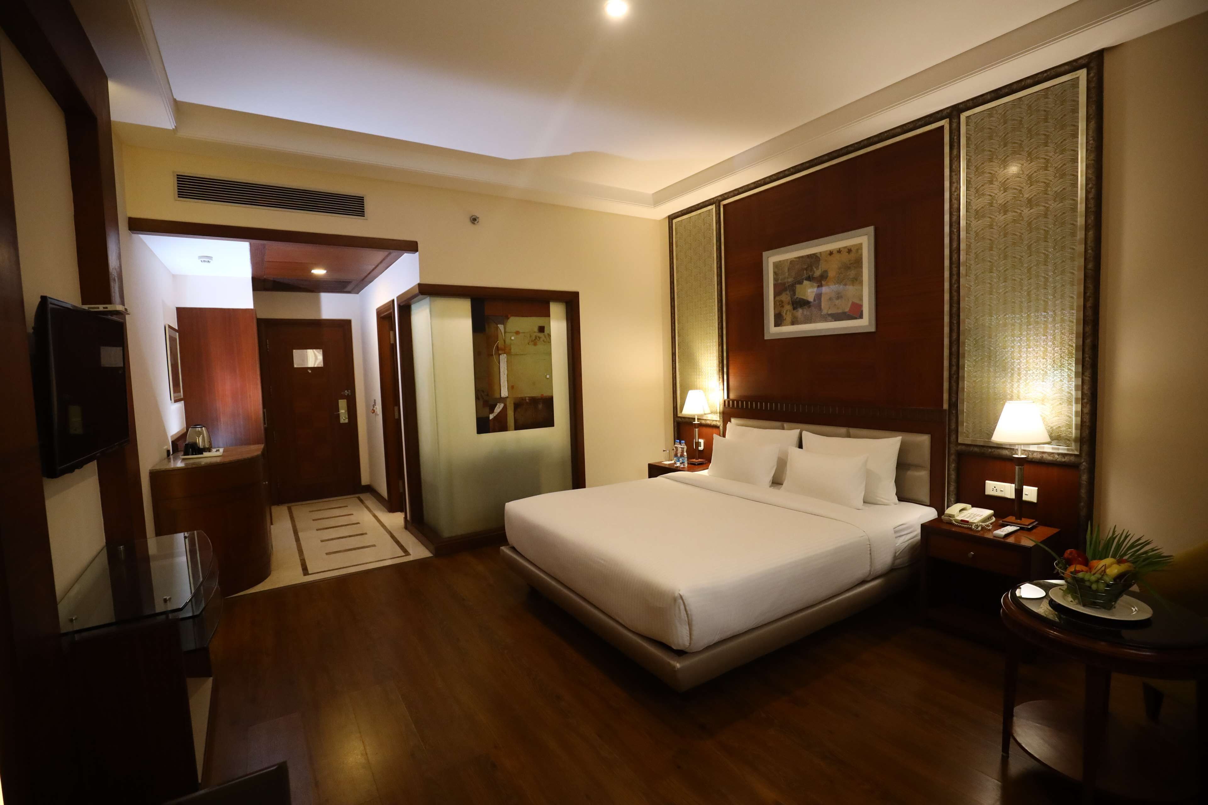 A hotel room with a large bed, bedside tables with lamps, a TV, and a wooden floor.