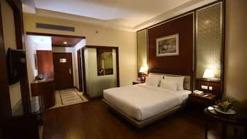 A hotel room with a large bed, bedside tables with lamps, a TV, and a wooden floor.