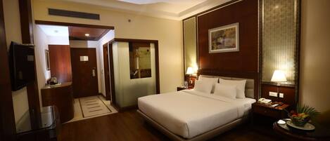 A hotel room with a large bed, bedside tables with lamps, a TV, and a wooden floor.