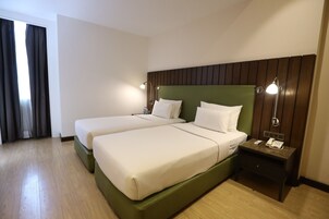 Een hotelkamer met twee bedden, een houten hoofdbord, bedlampen, een nachtkastje met een telefoon en een raam met gordijnen.