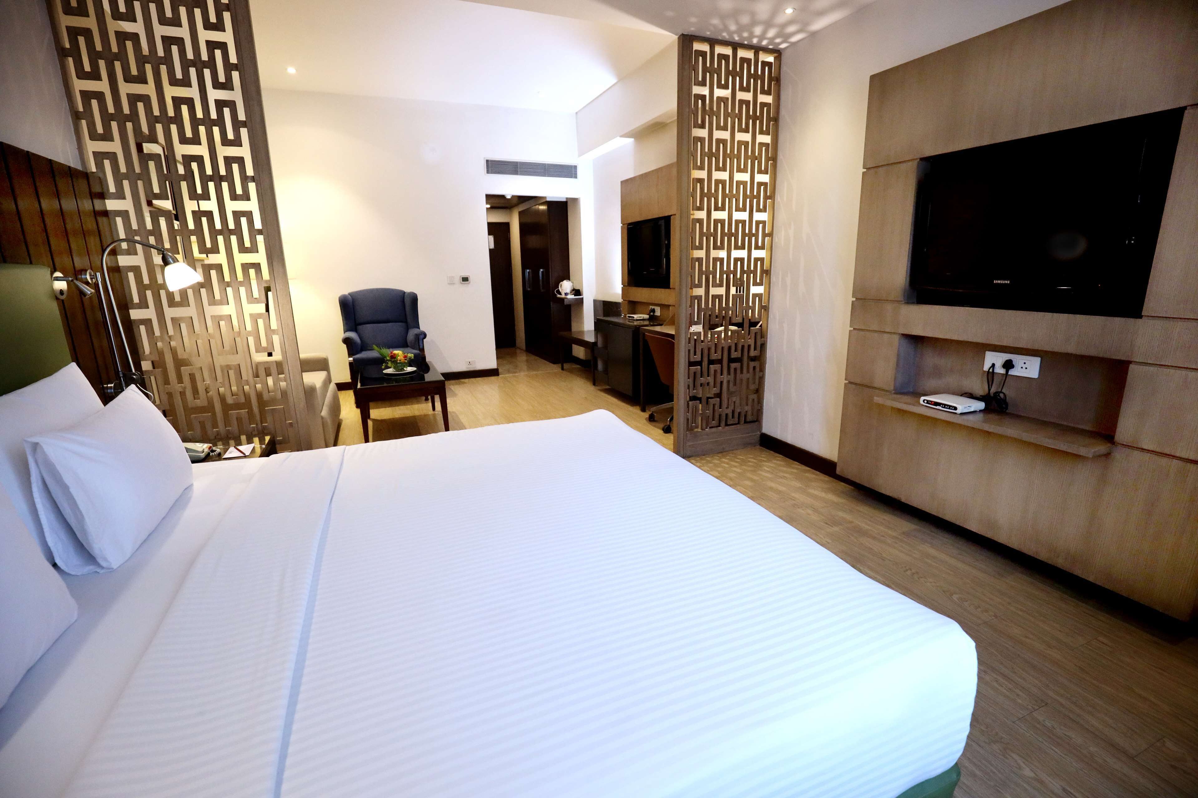 A hotel room with a large bed, a desk, a chair, a TV, and a decorative screen.