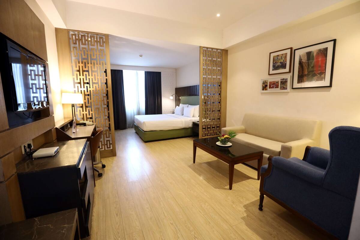Une chambre d’hôtel comprenant un lit, un bureau, un canapé, une télévision et un paravent décoratif.