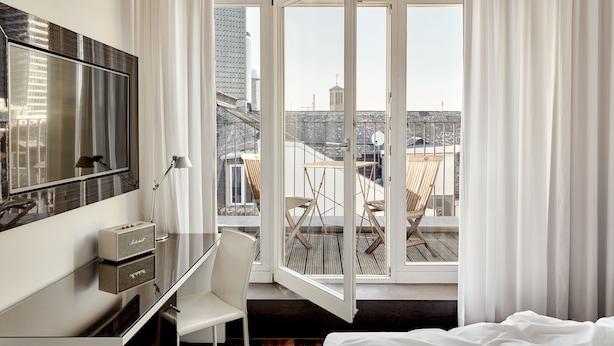 A hotel room with a large window, a desk with a flat-screen TV, a chair, and a bed. - The Pure, a Member of Design Hotels (Frankfurt)