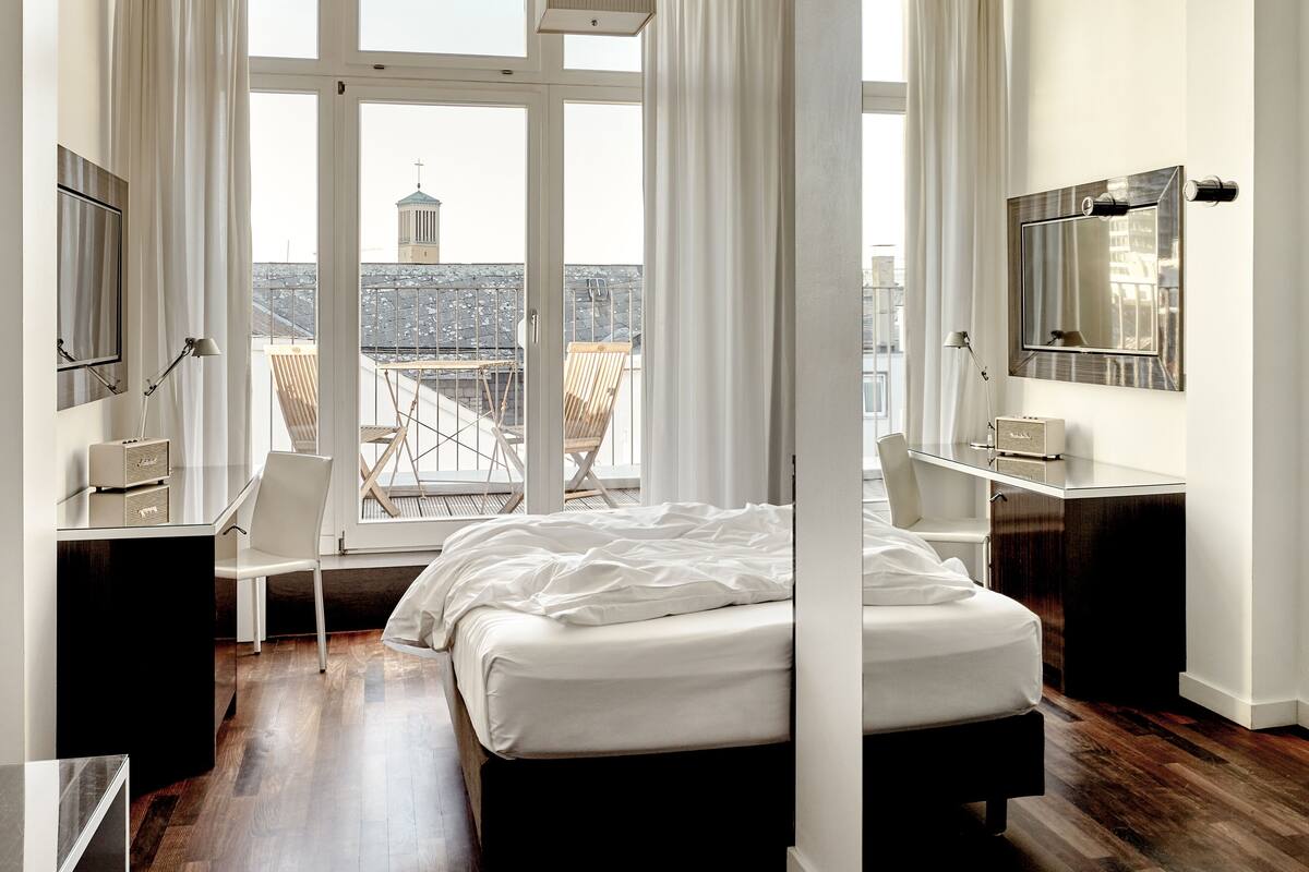 A modern hotel room with a large bed, a desk, a chair, and a TV.