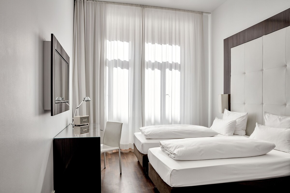 Une chambre d’hôtel moderne avec un grand lit, un bureau avec une chaise et un téléviseur fixé au mur.