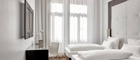 A modern hotel room with a large bed, a desk with a chair, and a television on the wall.