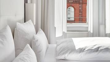 A hotel room with a bed, white curtains, and a view of a red brick building through a window.