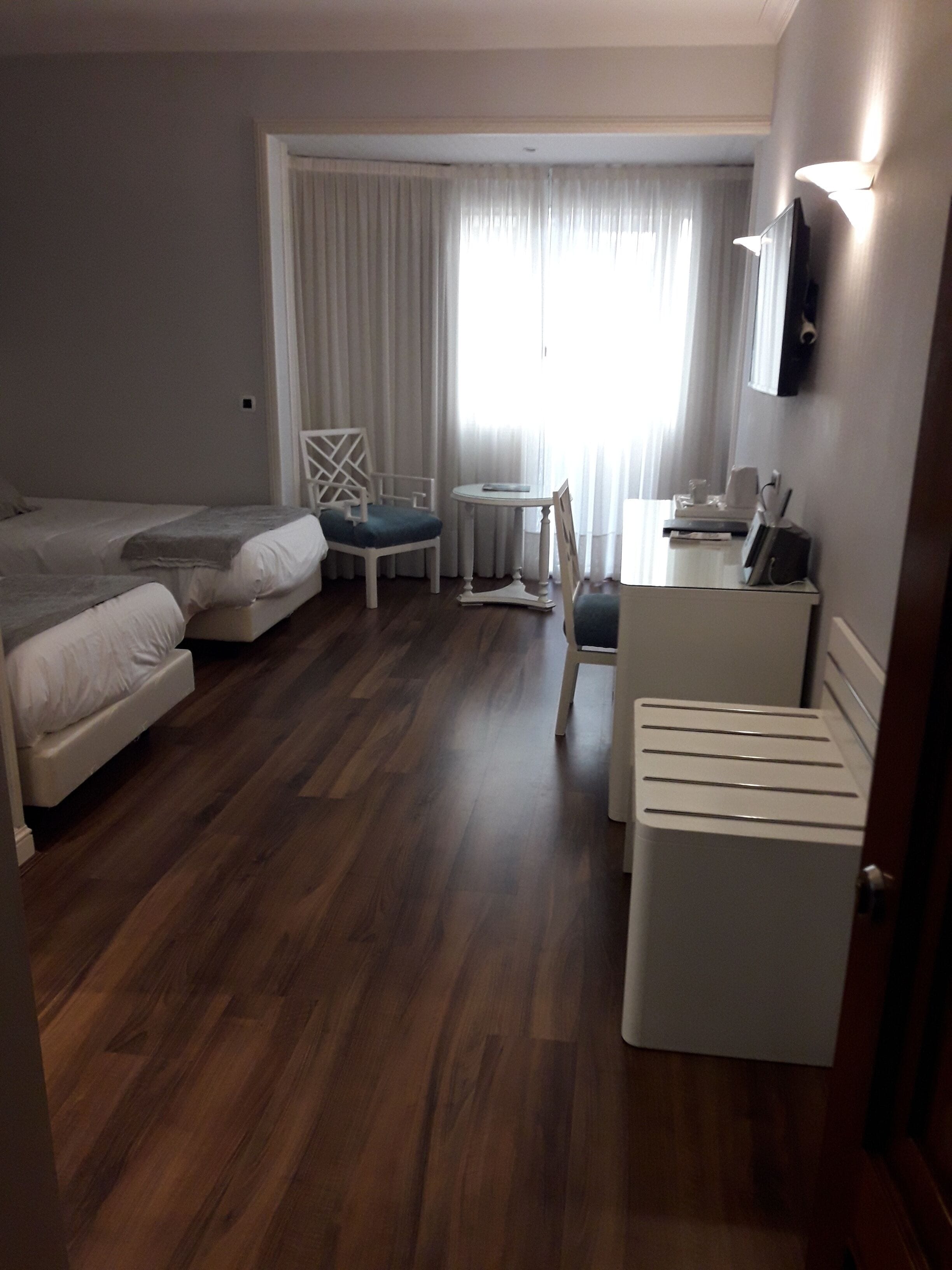 Habitación de hotel con dos camas, un escritorio, una silla, una mesita y un televisor.