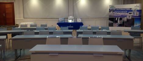 A conference room with rows of tables and chairs, a podium, and a presentation screen.