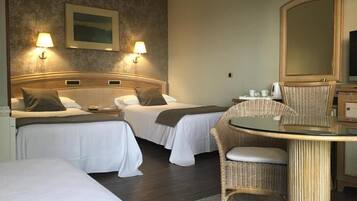 Habitació d'hotel amb dos llits, una taula rodona, una cadira de vimetla, un mirall i làmpades fixades a la paret.