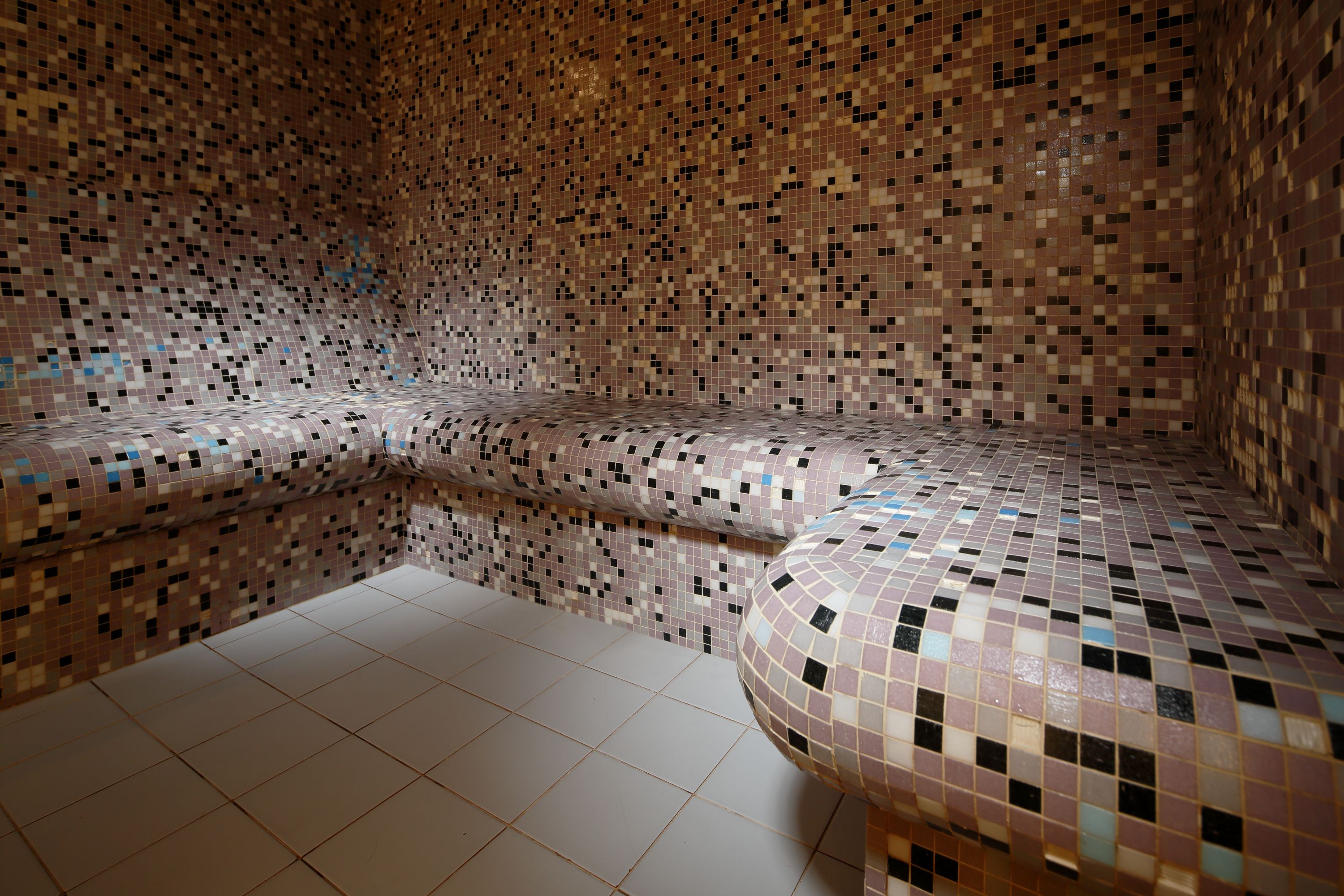 A room with a mosaic tiled wall, a bench, and a tiled floor.