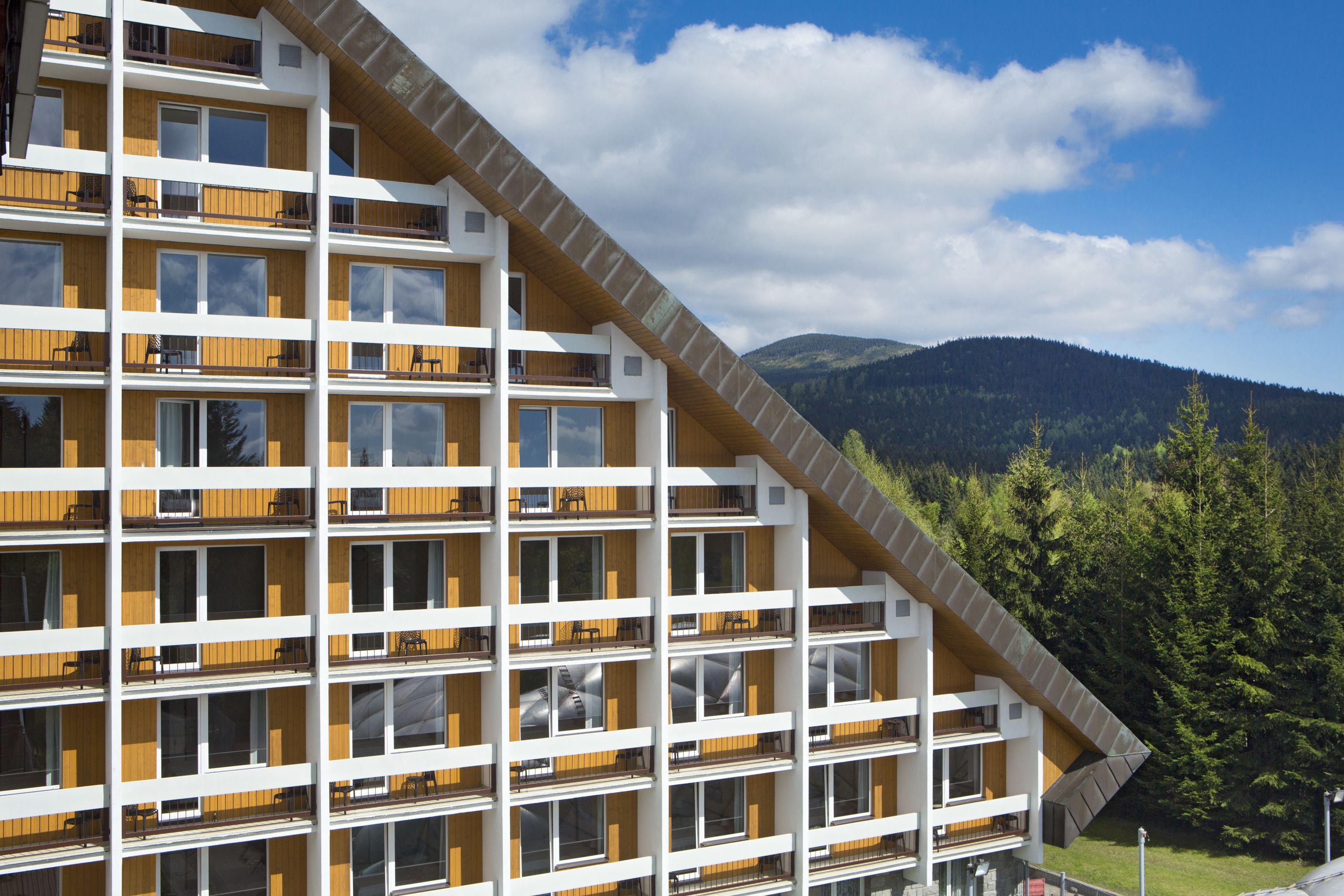 Un immeuble à plusieurs étages, doté de balcons, de grandes fenêtres et surplombant un paysage montagneux.