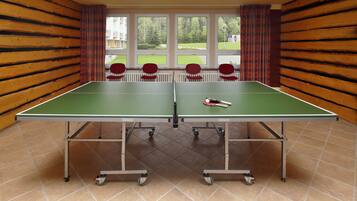 Une table de ping-pong avec quatre chaises rouges, une raquette de tennis de table et une balle.