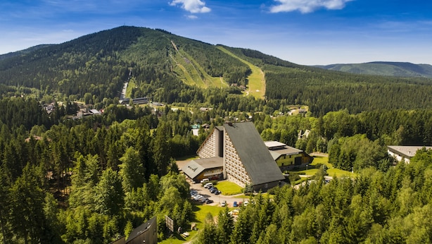 A mountain lodge with a prominent triangular roof, surrounded by dense forest and a ski slope in the background. - OREA Resort Sklář Harrachov (Harrachov)