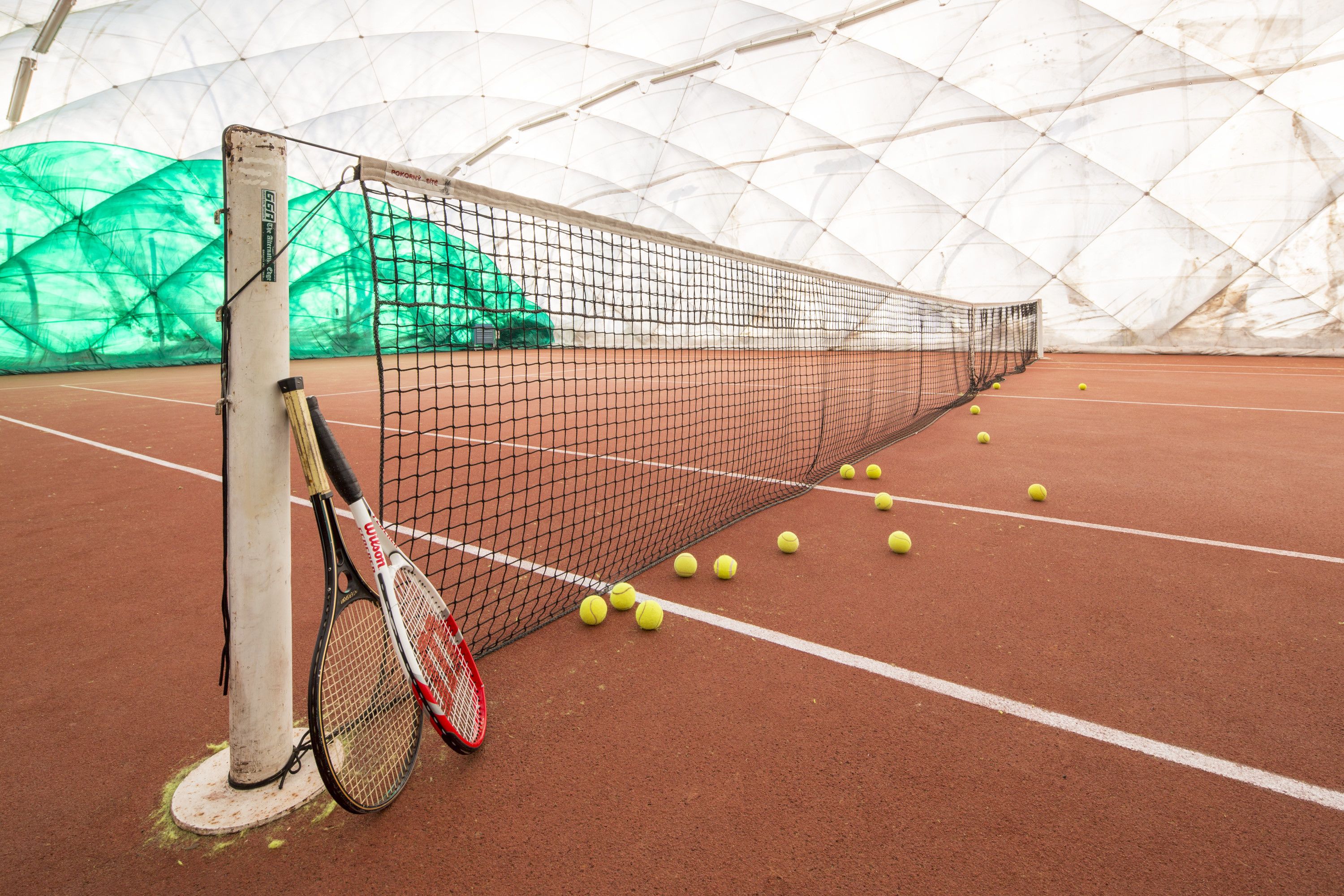 A tennis court with a net, tennis balls, and rackets.