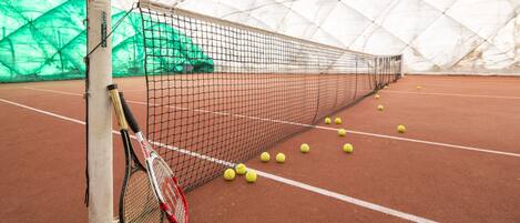 Cancha de tenis con red, pelotas y raquetas.