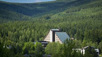 A large building with a sloped roof, surrounded by dense forest and hills.
