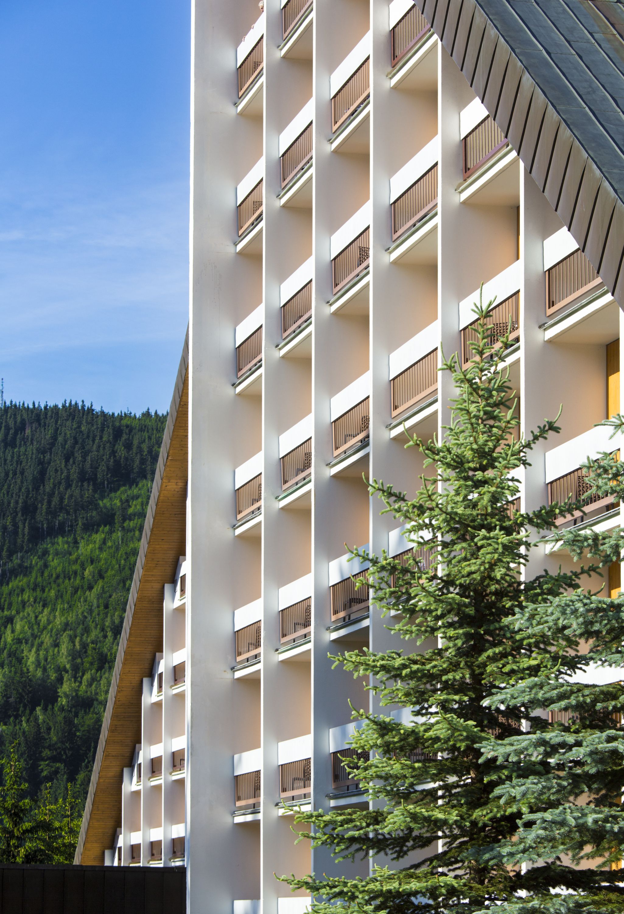 A multi-story building with balconies, surrounded by greenery and a forested hillside.
