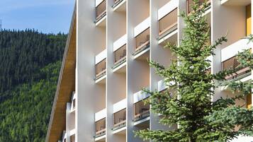 A multi-story building with balconies, surrounded by greenery and a forested hillside.