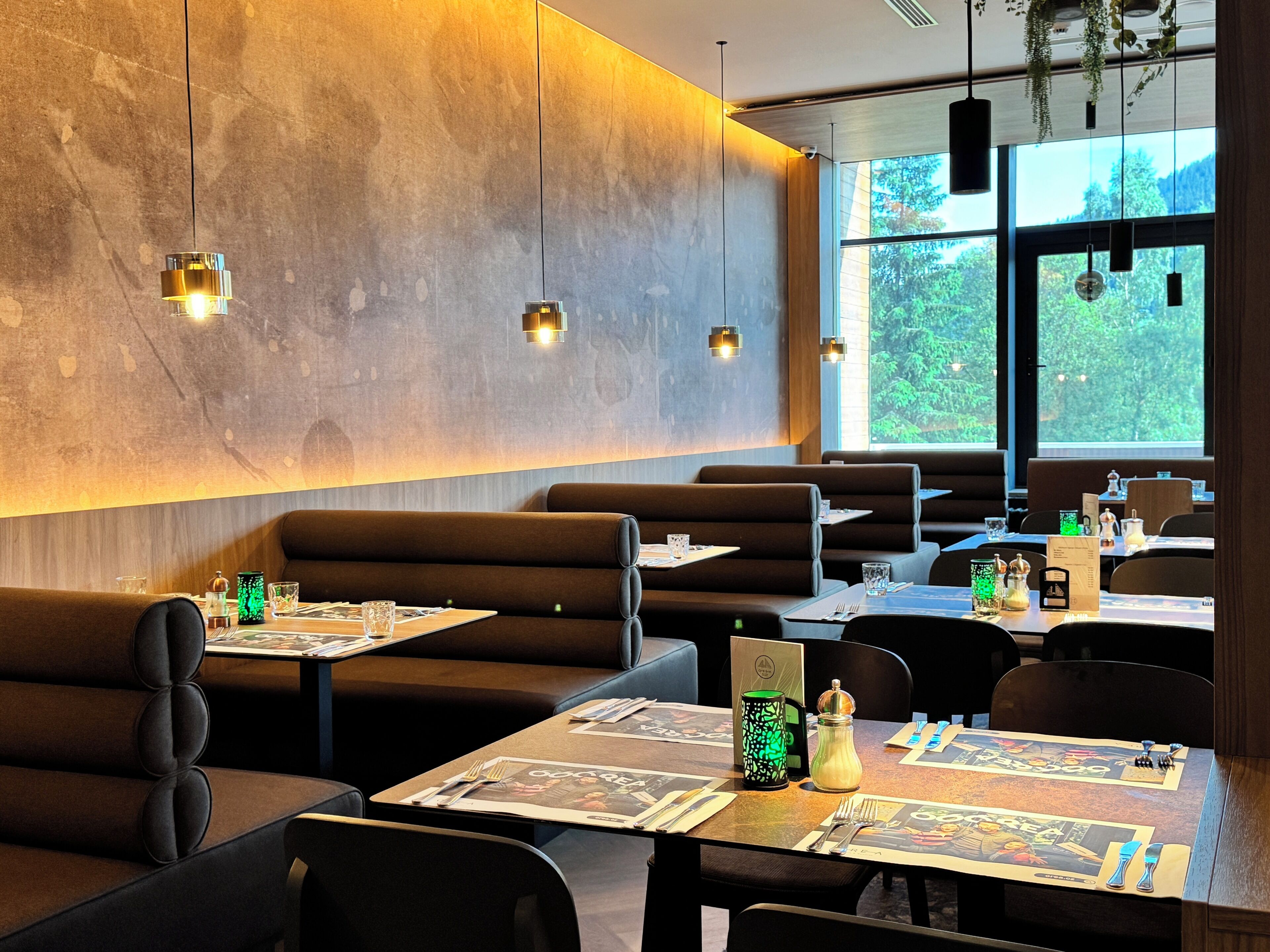 Un interior de restaurante moderno con asientos tipo cabina, mesas con menús e iluminación colgante.